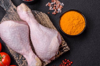 Tuzlu, baharatlı ve otlu çiğ tavuk budu. Koyu beton arka planda pişirmeye hazır.