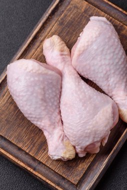 Tuzlu, baharatlı ve otlu çiğ tavuk budu. Koyu beton arka planda pişirmeye hazır.