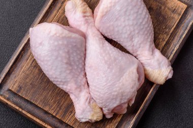 Tuzlu, baharatlı ve otlu çiğ tavuk budu. Koyu beton arka planda pişirmeye hazır.