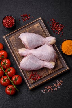 Tuzlu, baharatlı ve otlu çiğ tavuk budu. Koyu beton arka planda pişirmeye hazır.