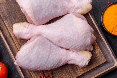 Tuzlu, baharatlı ve otlu çiğ tavuk budu. Koyu beton arka planda pişirmeye hazır.