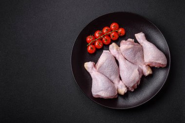 Tuzlu, baharatlı ve otlu çiğ tavuk budu. Koyu beton arka planda pişirmeye hazır.