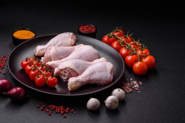 Tuzlu, baharatlı ve otlu çiğ tavuk budu. Koyu beton arka planda pişirmeye hazır.