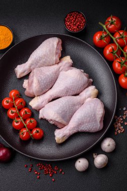 Tuzlu, baharatlı ve otlu çiğ tavuk budu. Koyu beton arka planda pişirmeye hazır.