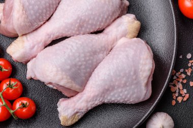 Tuzlu, baharatlı ve otlu çiğ tavuk budu. Koyu beton arka planda pişirmeye hazır.