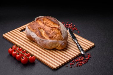 Tahta kesme tahtasının üzerinde tahıl taneleriyle birlikte koyu beton arka planda bir somun kahverengi ekmek.