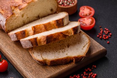Tahta kesme tahtasının üzerinde tahıl taneleriyle birlikte koyu beton arka planda bir somun kahverengi ekmek.