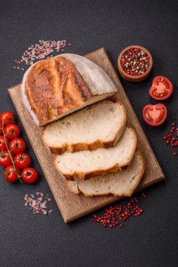 Tahta kesme tahtasının üzerinde tahıl taneleriyle birlikte koyu beton arka planda bir somun kahverengi ekmek.
