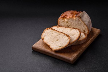 Tahta kesme tahtasının üzerinde tahıl taneleriyle birlikte koyu beton arka planda bir somun kahverengi ekmek.