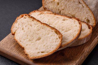 Tahta kesme tahtasının üzerinde tahıl taneleriyle birlikte koyu beton arka planda bir somun kahverengi ekmek.