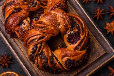 Lezzetli taze haşlanmış çörek, haşhaş tohumları ve koyu beton arka planda halka şeklinde böğürtlenler.