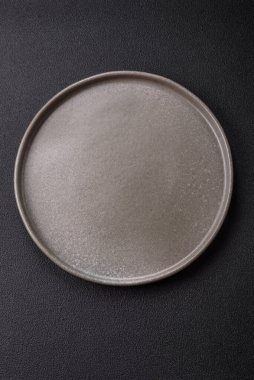 Empty ceramic round plate on dark textured concrete background. Cutlery, preparation for dinner