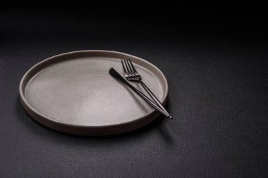 Empty ceramic round plate on dark textured concrete background. Cutlery, preparation for dinner