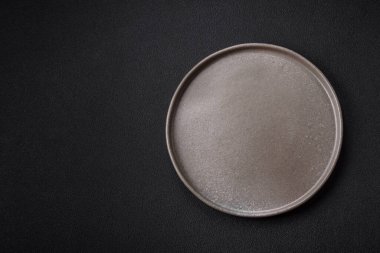 Empty ceramic round plate on dark textured concrete background. Cutlery, preparation for dinner