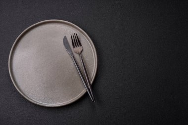 Empty ceramic round plate on dark textured concrete background. Cutlery, preparation for dinner