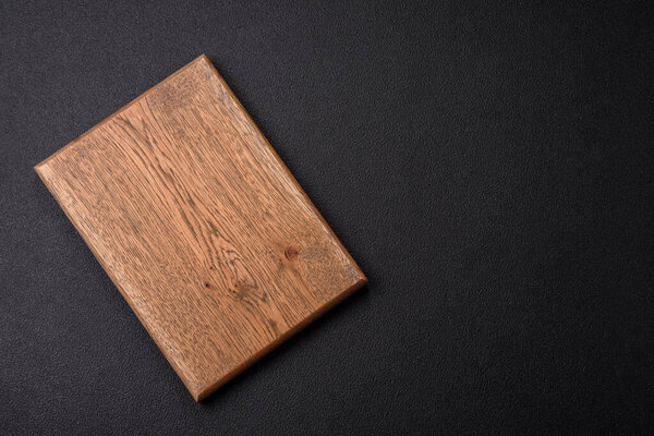Empty wooden cutting board on dark textured concrete background. Cutlery, preparation for dinner