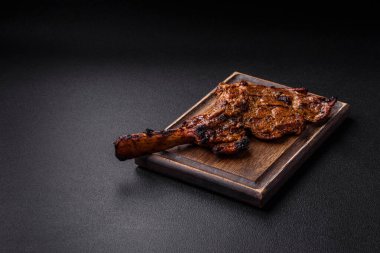 Izgarada pişirilmiş kemiğin üzerinde sulu etli baltalı biftek ve koyu beton arka planda tuz ve baharatlar.