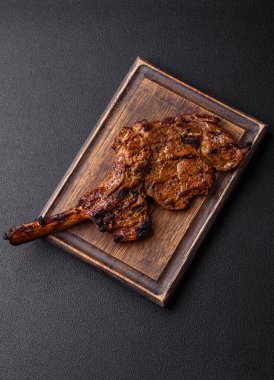 Izgarada pişirilmiş kemiğin üzerinde sulu etli baltalı biftek ve koyu beton arka planda tuz ve baharatlar.