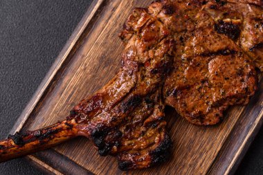 Izgarada pişirilmiş kemiğin üzerinde sulu etli baltalı biftek ve koyu beton arka planda tuz ve baharatlar.