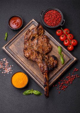 Izgarada pişirilmiş kemiğin üzerinde sulu etli baltalı biftek ve koyu beton arka planda tuz ve baharatlar.
