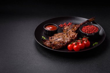 Izgarada pişirilmiş kemiğin üzerinde sulu etli baltalı biftek ve koyu beton arka planda tuz ve baharatlar.