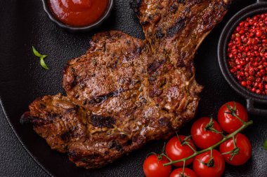 Izgarada pişirilmiş kemiğin üzerinde sulu etli baltalı biftek ve koyu beton arka planda tuz ve baharatlar.