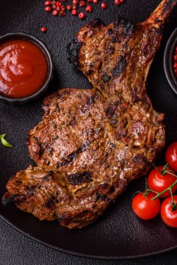 Izgarada pişirilmiş kemiğin üzerinde sulu etli baltalı biftek ve koyu beton arka planda tuz ve baharatlar.