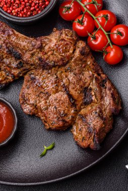 Izgarada pişirilmiş kemiğin üzerinde sulu etli baltalı biftek ve koyu beton arka planda tuz ve baharatlar.