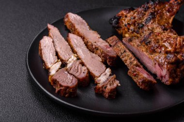 Izgarada pişirilmiş kemiğin üzerinde sulu etli baltalı biftek ve koyu beton arka planda tuz ve baharatlar.