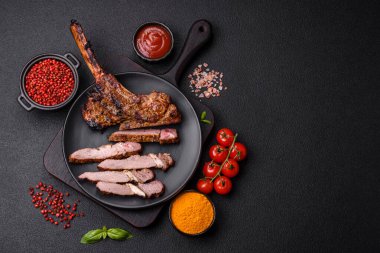 Izgarada pişirilmiş kemiğin üzerinde sulu etli baltalı biftek ve koyu beton arka planda tuz ve baharatlar.