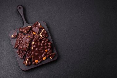 Fındıklı siyah acı çikolata, şekerli meyve ve nane. Koyu beton bir arka planda parçalara ayrılmış.