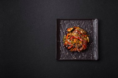 Baharatlı Asya yemeği dilimlenmiş et filetosu, acı biber, havuç ve susam tohumları koyu beton arka planda.