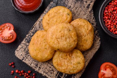 Yuvarlak balık veya tuzlu tavuk nuggetları ve koyu beton arka planda ekilmiş baharatlar.