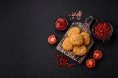 Yuvarlak balık veya tuzlu tavuk nuggetları ve koyu beton arka planda ekilmiş baharatlar.