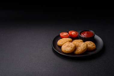 Yuvarlak balık veya tuzlu tavuk nuggetları ve koyu beton arka planda ekilmiş baharatlar.