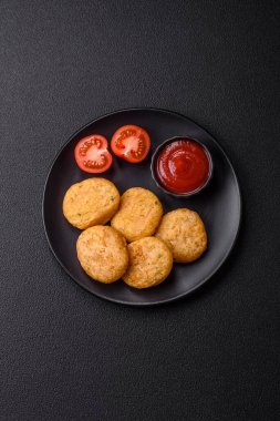 Yuvarlak balık veya tuzlu tavuk nuggetları ve koyu beton arka planda ekilmiş baharatlar.