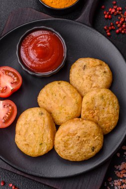 Yuvarlak balık veya tuzlu tavuk nuggetları ve koyu beton arka planda ekilmiş baharatlar.