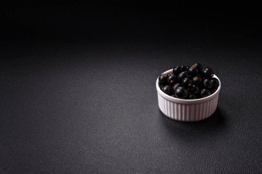 Olgun kuşüzümü, koyu beton arka planda seramik bir kasede su damlacıkları içinde.