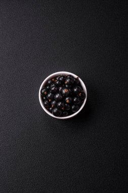 Olgun kuşüzümü, koyu beton arka planda seramik bir kasede su damlacıkları içinde.