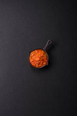 Kırmızı acı ya da baharatlı biberli, domatesli, sarımsaklı, baharatlı ve otlu koyu beton arka planda.