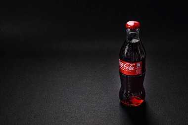 Nikopol, Dnepropetrovsk bölgesi / Ukrayna - 15 Temmuz 2024: Siyah zemin üzerinde su damlaları bulunan bir şişe soğutulmuş koka-kola. Sıcak bir yaz gününde serin bir içecek.