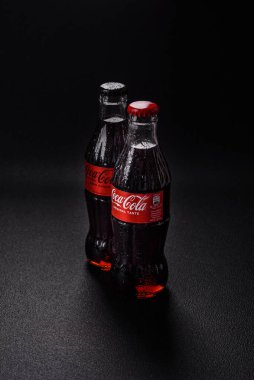 Nikopol, Dnepropetrovsk bölgesi / Ukrayna - 15 Temmuz 2024: Siyah zemin üzerinde su damlaları bulunan bir şişe soğutulmuş koka-kola. Sıcak bir yaz gününde serin bir içecek.