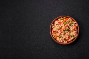 Lezzetli haşlanmış pirinç, sebzeli havuç, bezelye, tuz ve baharatla birlikte koyu beton arka planda.