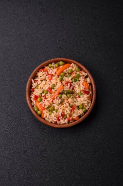 Lezzetli haşlanmış pirinç, sebzeli havuç, bezelye, tuz ve baharatla birlikte koyu beton arka planda.