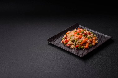 Lezzetli haşlanmış pirinç, sebzeli havuç, bezelye, tuz ve baharatla birlikte koyu beton arka planda.