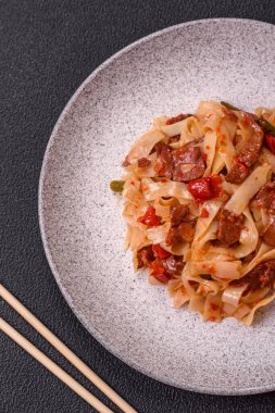 Sebzeli, etli, tuzlu ve baharatlı nefis Asya udonu tabağı koyu beton arka planda seramik bir tabakta.