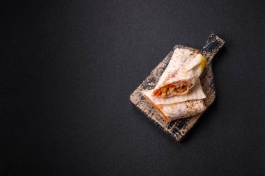 Lezzetli sulu rulo ya da tavuklu shawarma, domates, salata ve soslu koyu beton arka planda