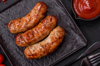 Koyu beton arka planda tuzlu, baharatlı ve otlu kızarmış domuz veya tavuk sosisi.
