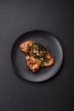 Koyu beton bir arka planda tuzlu, baharatlı ve otlu ızgara kemiksiz tavuk budu.