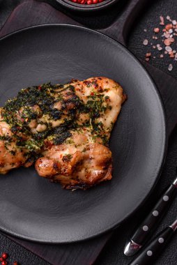 Koyu beton bir arka planda tuzlu, baharatlı ve otlu ızgara kemiksiz tavuk budu.
